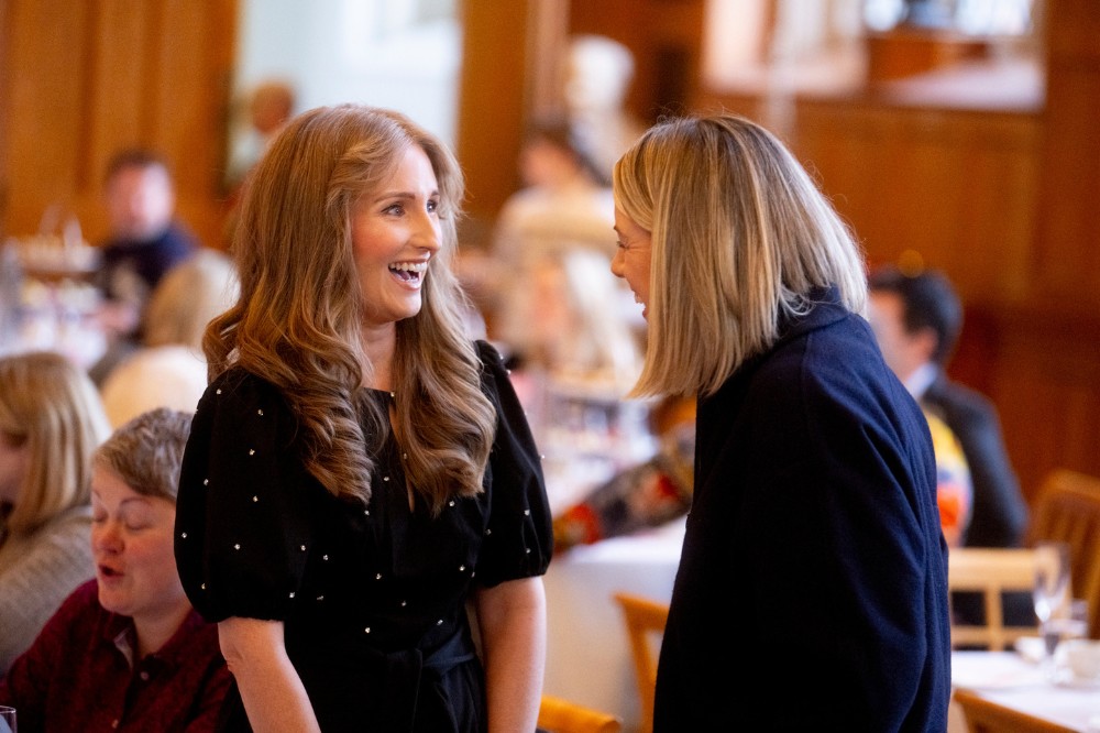 two women smiling and chatting happily at and indoor event