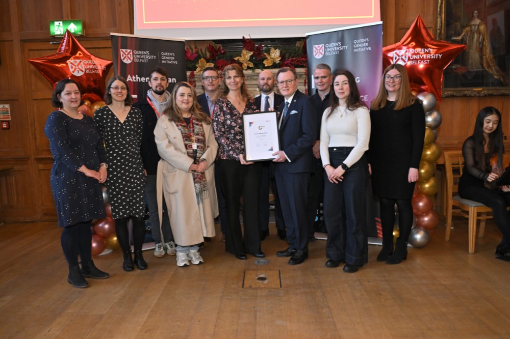 group of people posing with a framed award certificate in an old event hall with presentation screen, pop-up stands and balloon pillars in the background