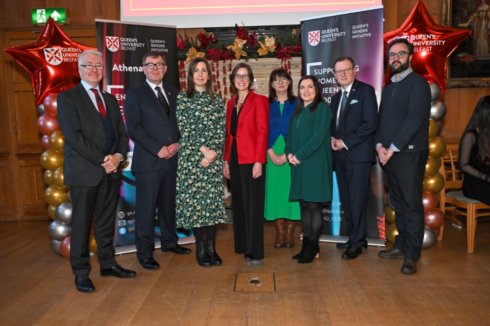 group of four men and four women posing for a photo in an old wood-paneled event hall with pop-up stands and presentation screen in the background