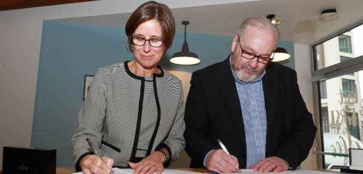 A woman and man sign documents at a college campus
