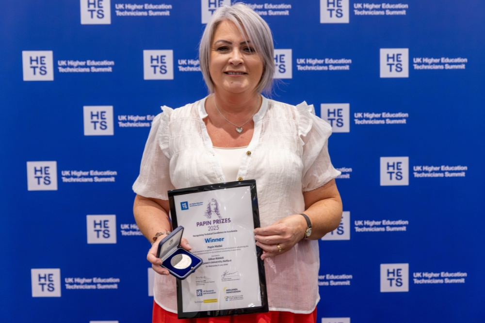 Gillian Riddell smiling as she receives the Papin Medal Award on stage, holding the medal