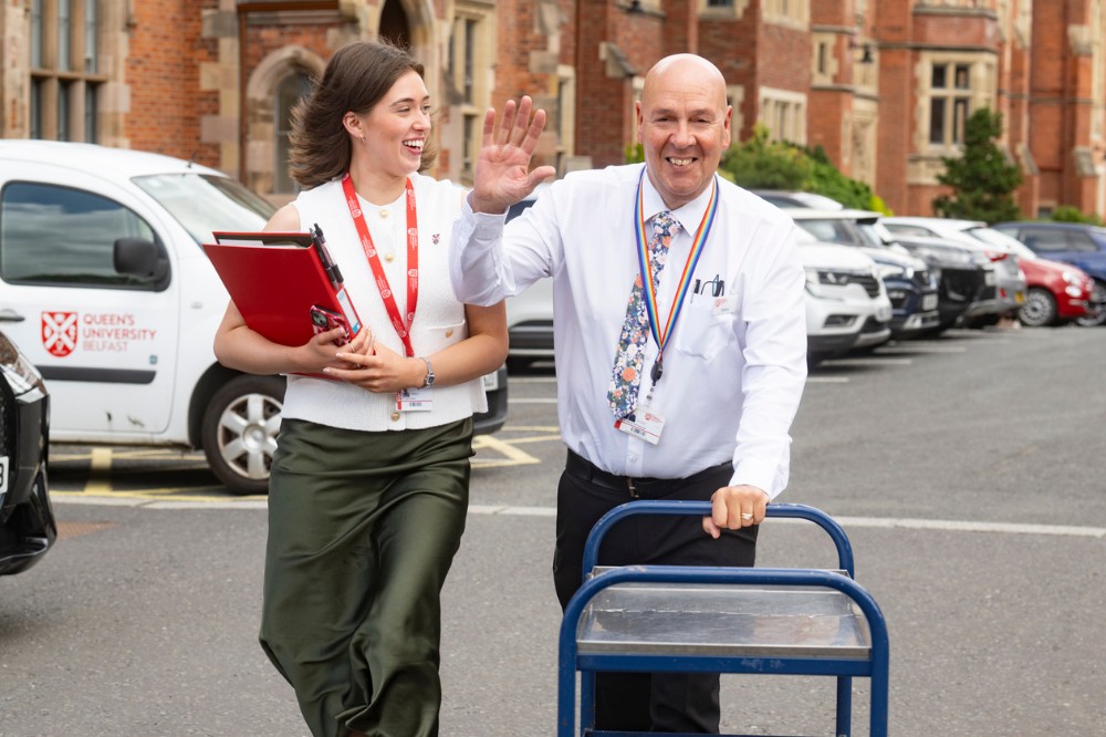 smiling woman holding A4 notepad or clipboard walking beside a smiling man pushing a catering trolley