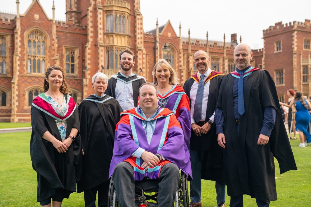 group of academics - one in a wheelchair - in graduation robes on the lawn of a redbrick building