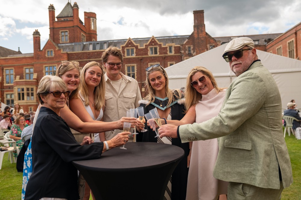 smiling family group standing at a small table in the quadrangle of a redbrick building