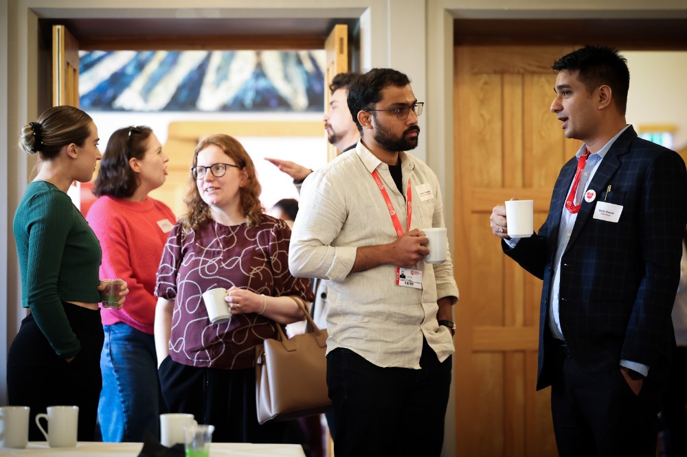 women and men standing and chatting over coffee at an event in a comfortable-looking meeting space