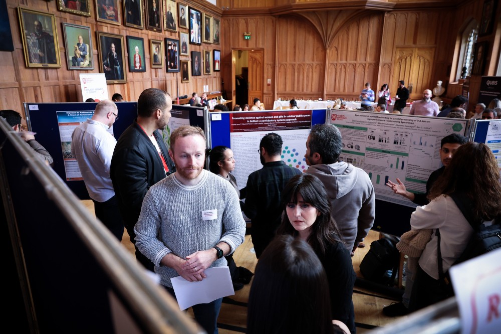 large group of people standing and conversing at a research poster exhibition in a grand, wood-paneled event space with portraits hanging on the walls