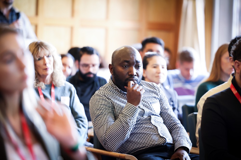seated group of people in a comfortable-looking, wood-paneled meeting space listening to a presentation
