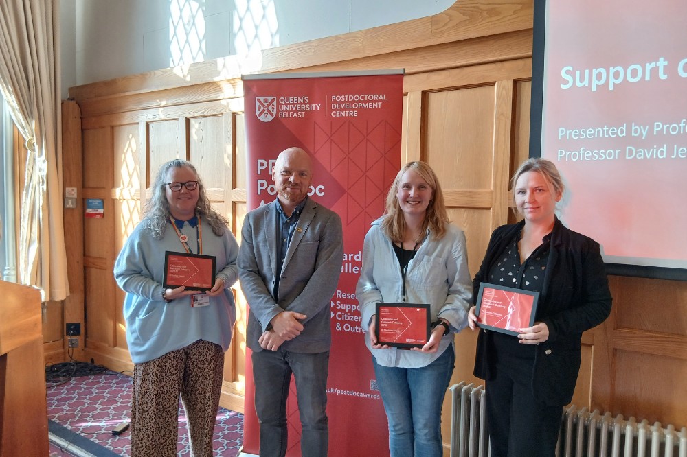 four people, three holding award certificates, at an indoor event in a wood-paneled room
