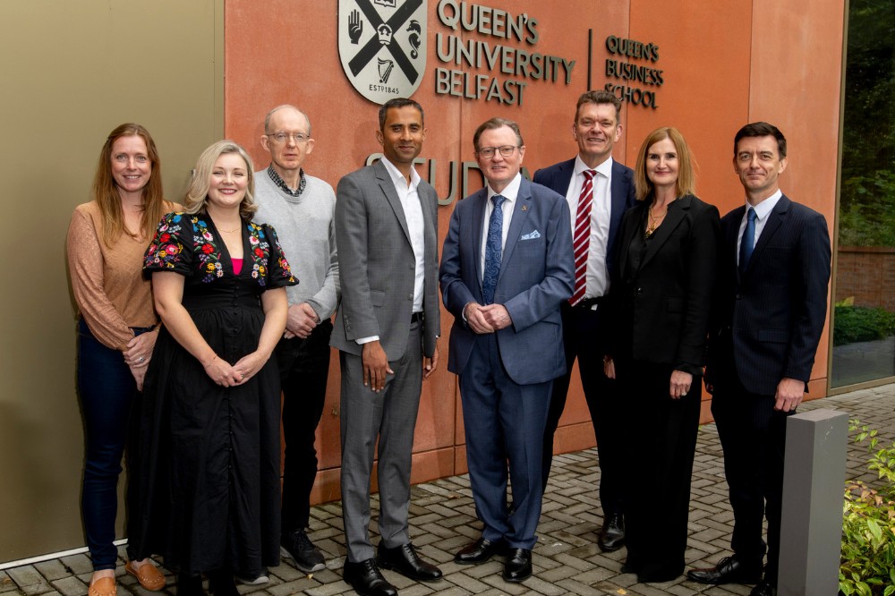 three women and five men in business dress posing for the camera outside Queen's Business School Student Hub, Queen's University Belfast