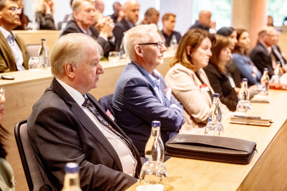 group of serious-looking senior professionals seated and listening at an event in a bright lecture space
