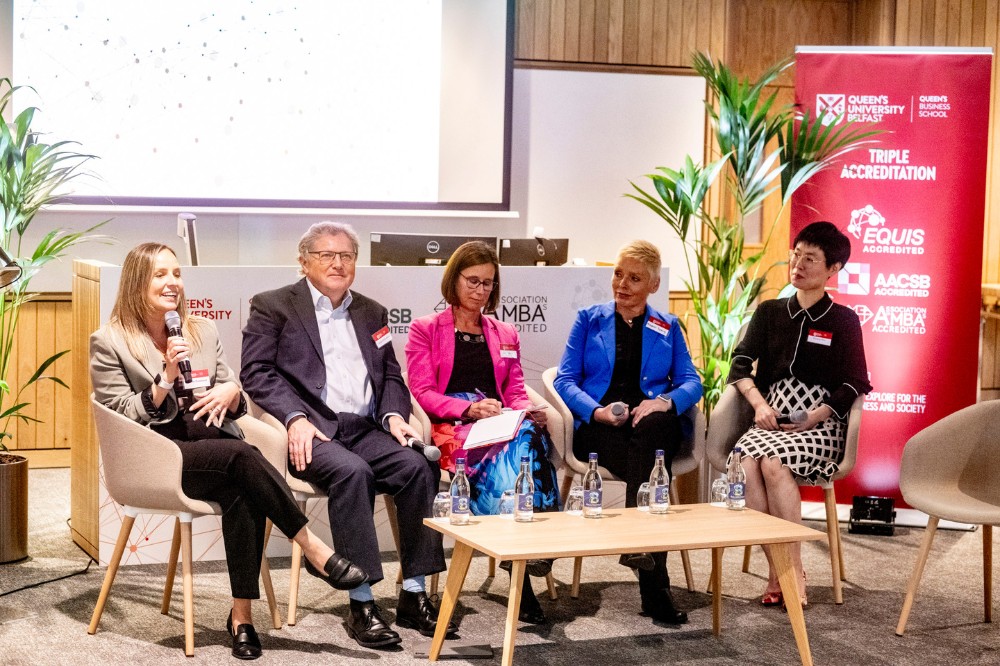 group of one male and four female panelists seated at an event - the panelist on the left is speaking into a mic