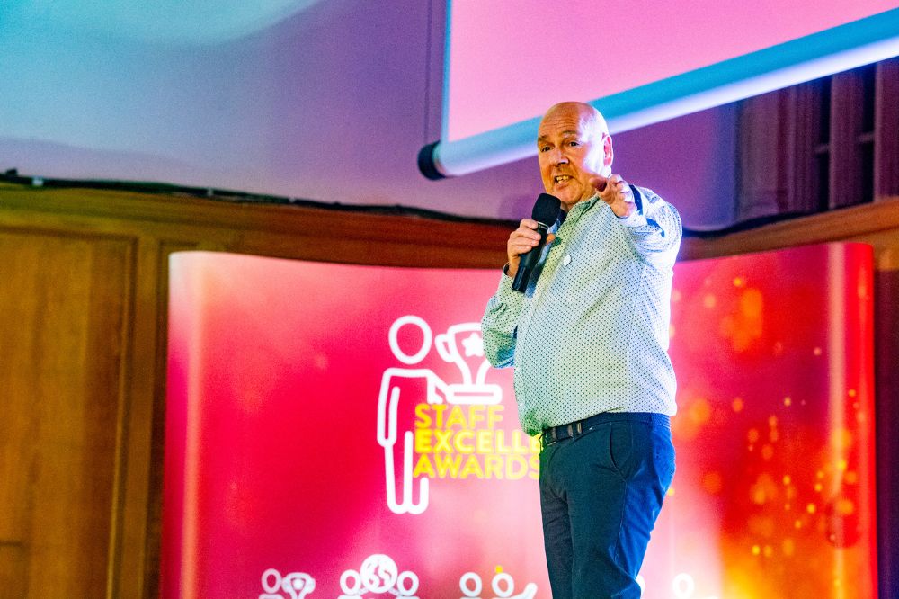 man in light-coloured shirt speaking or singing into a microphone on a stage