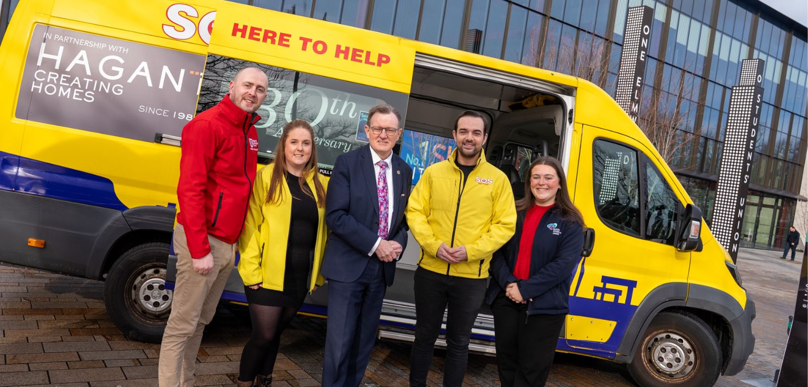 Image shows five people standing in front of a yellow bus.