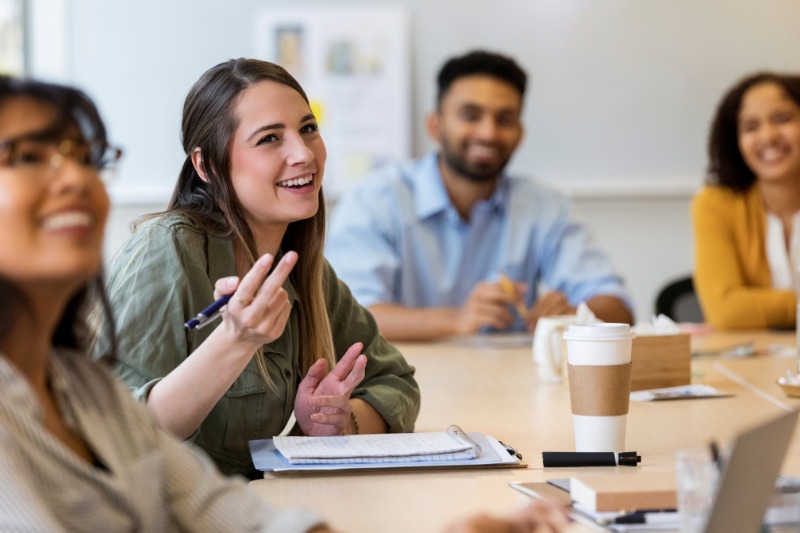 smiling young woman speaking at a table with colleagues in an informal meeting setting