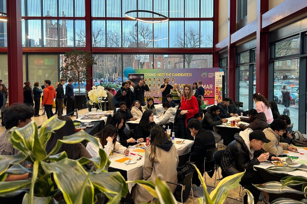 young people seated and in discussion at tables, and other people standing in the background, in the atrium of a modern glass-fronted building