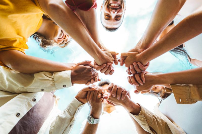 group of people holding hands in a circle - photo is taken from near the ground looking up